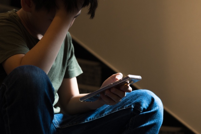 Niño triste mirando el celular sentado en la escalera